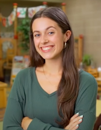 Izzy smiling with arms crossed in classroom on UO campus