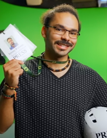 Jeremy holding press pass and helment in front of green screen on UO campus