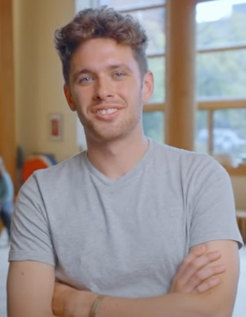 Jonah smiling crossed arm in the Many Nations Longhouse on UO campus