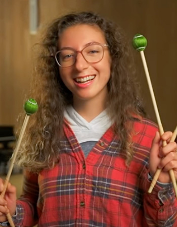 Natalie smiling and holding percussion sticks in music school on UO campus