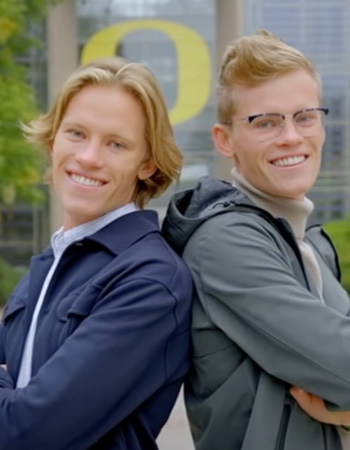 Riley and Bretten posing back to back in front of Lillis on UO campus