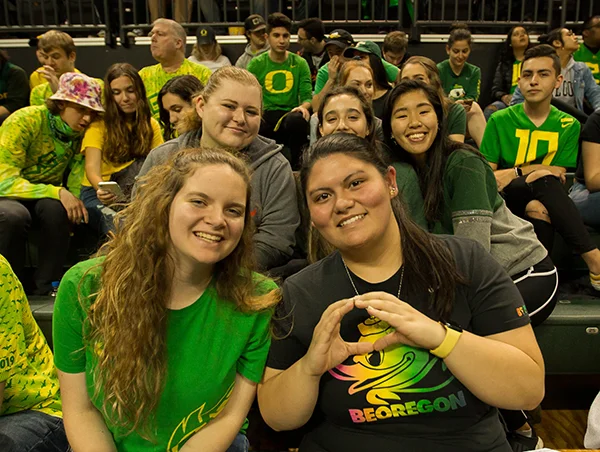 Students sitting at Duck Athletic game and smiling at camera